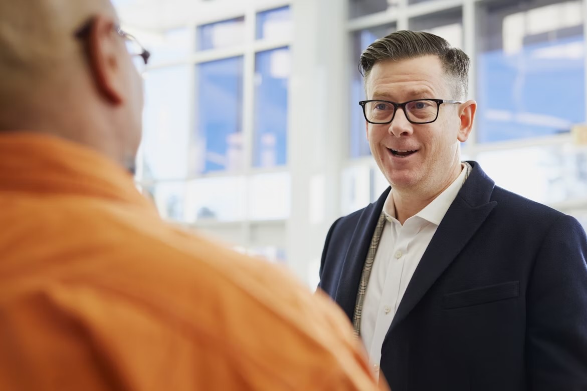 A man in a suit talking with a man in an orange shirt
