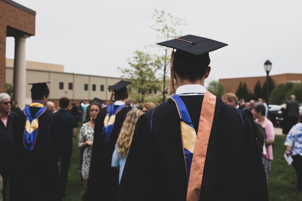 A bunch of graduates cap and gown standing in a school yard with family