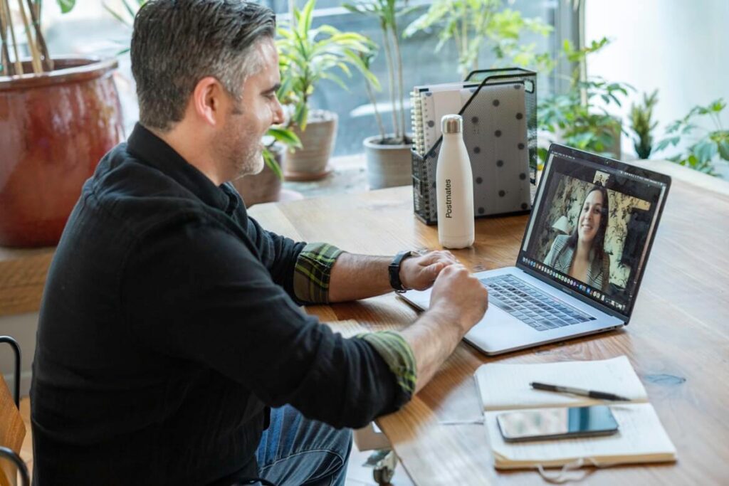 A man on a video call with a woman on his laptop, a notebook sitting on the table beside him