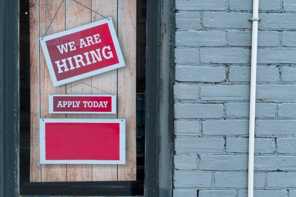 A doorway with a red sign that reads “WE ARE HIRING” and “APPLY TODAY”