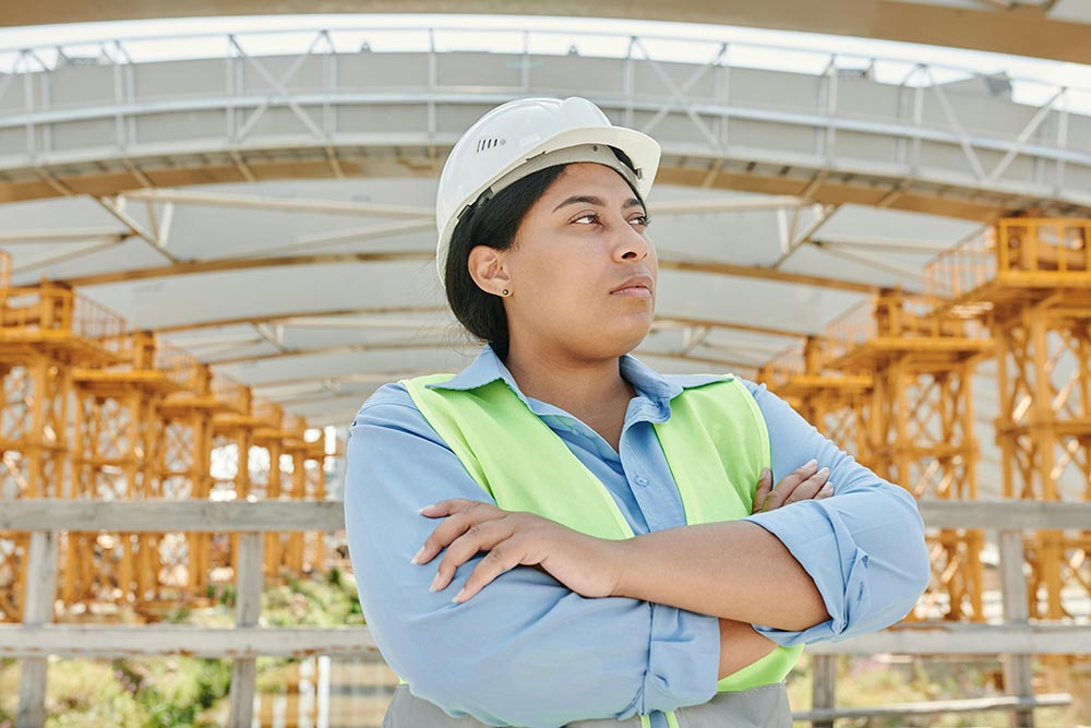 A professional woman in a high visibility vest and a hard hat, looking confident