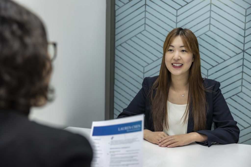 A professional looking young woman sitting across another person in glasses, holding a resume