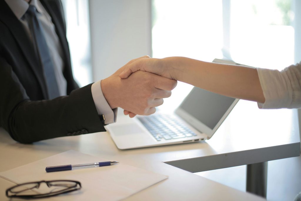 A person in a suit shaking hands with someone over top of a desk