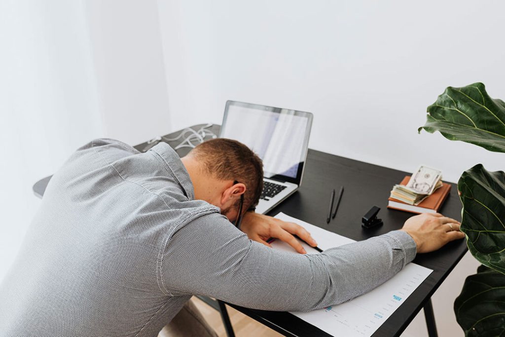 A person looking distraught about their computer, laying on their desk