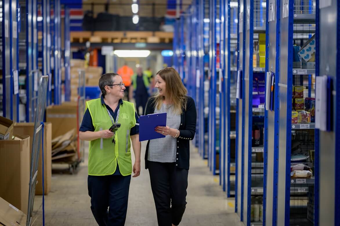 Two workers walking through a warehouse with a clipboard and scanning device