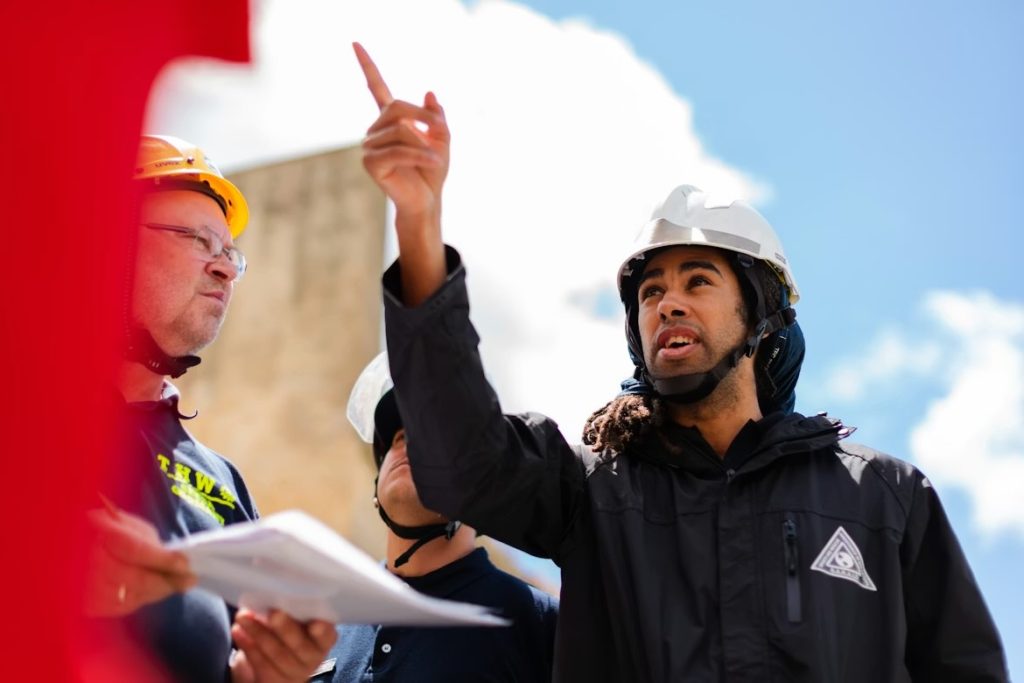 A man in a white helmet standing on a construction site pointing near other workers