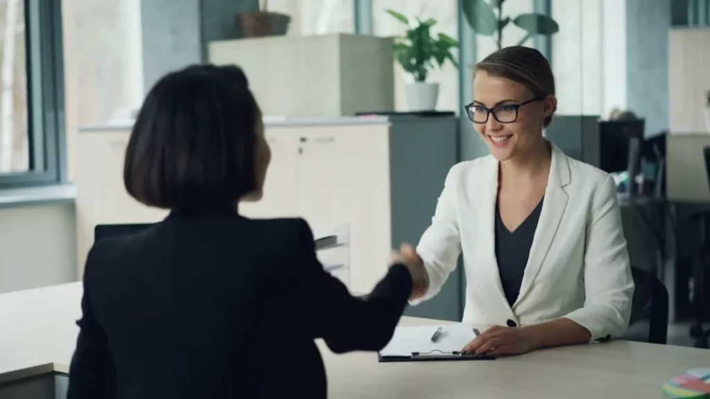 Two professional looking women shaking hands over an office desk