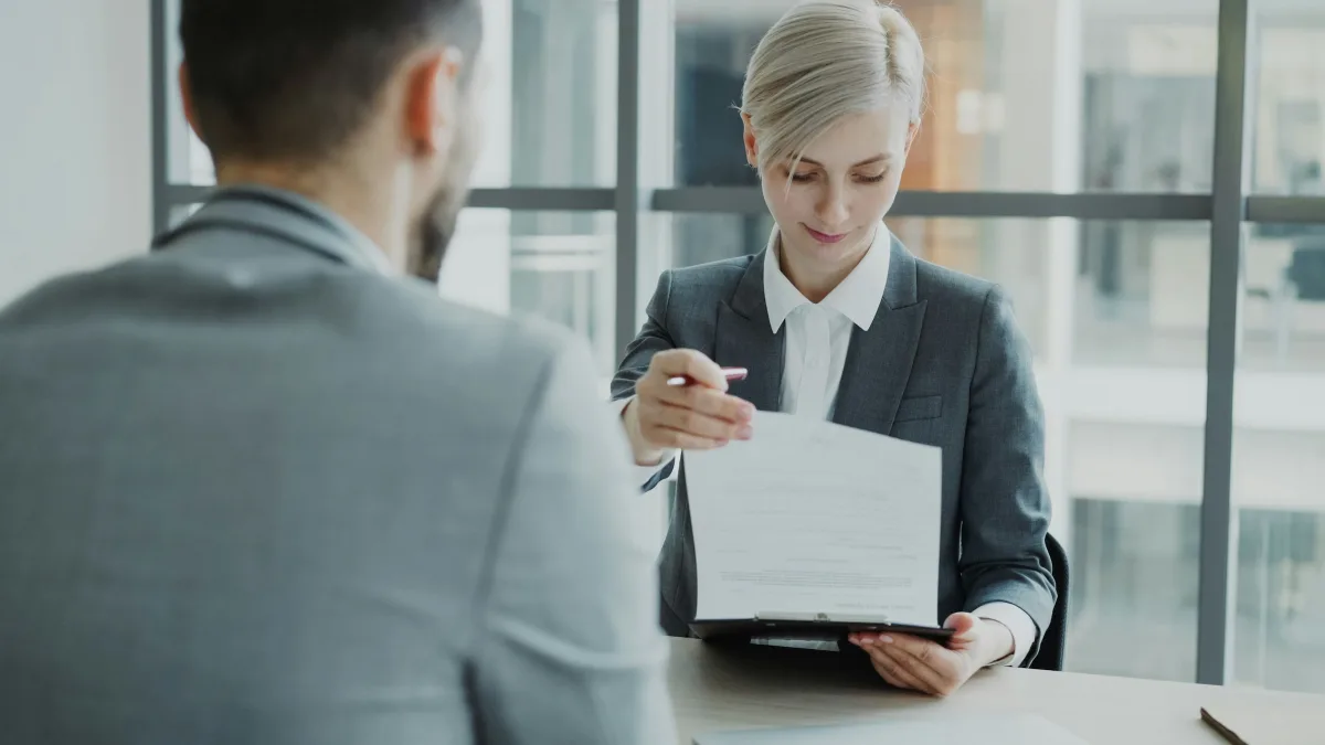 A man sitting across from a woman reading over a clipboard.